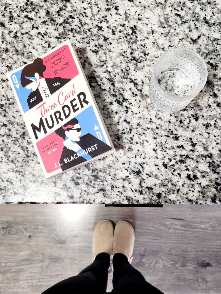 cover of three card murder on a countertop with a glass of water